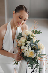 Portrait beautiful Bride Admiring Her Bouquet of Cream Roses and Eucalyptus. Elegant young woman with classic hairstyle and makeup on wedding celebration