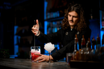 Focus on a cocktail mixing glass in which a bartender stirs an alcoholic drink with ice with a bar spoon