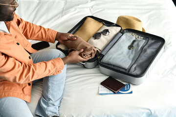 High angle closeup of Black man packing suitcase preparing for travel in hotel room copy space