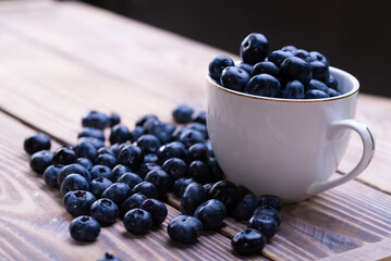 Fresh blueberries in a white cup on a wooden table