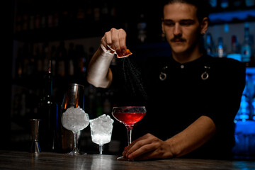 Bartender squeezes a piece of peel over the cocktail so that the splashes from it fly into the cocktail