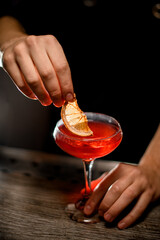 Bartender holding a stem of a cocktail glass with one hand and dipping a lemon wedge into the cocktail