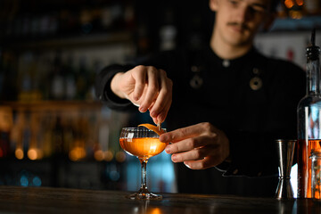 Bartender attaches a piece of zest with a clothespin to a glass filled with a brown cocktail