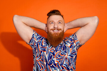 Photo of dreamy sweet guy dressed print shirt arms behind head looking up empty space isolated orange color background