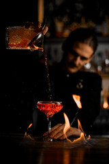 Focus on a cocktail glass standing in flames on the bar