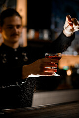 Bartender holding glass with cocktail in front of him and being sprayed with spray