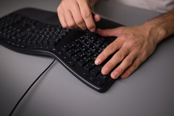 In a closeup shot, a hand is seen using a keycap puller tool to meticulously remove a keyboard key