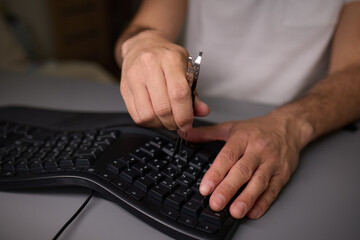 In a closeup shot, a hand is seen using a keycap puller tool to meticulously remove a keyboard key