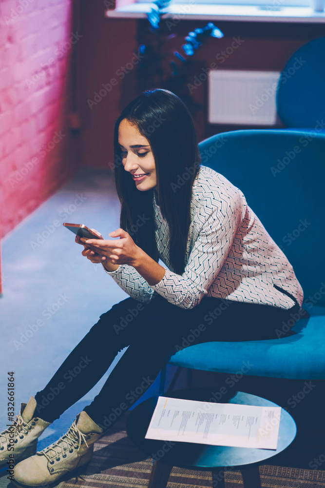 Aufkleber smiling hipster girl blogging in networks and reading news via smartphone during free time in cowork