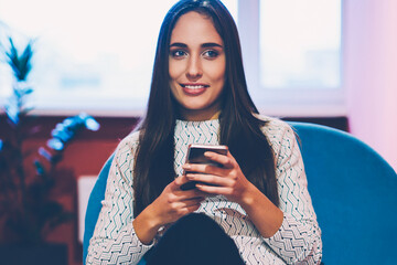 Positive brunette woman using mobile phone for networking on work break in office,young hipster...