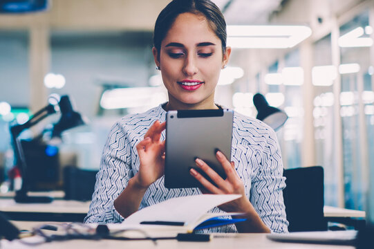 Skilled female employee making research via digital tablet analyzing information from network creating project,woman reading income message checking mail via portable pc sitting at desktop in office