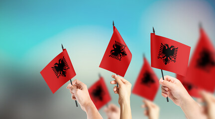 A group of people are holding small flags of Albania in their hands.