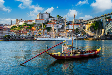 Obraz premium View of Porto city and Douro river with traditional boats with port wine barrels and sailing ship from famous tourist viewpoint Marginal de Gaia riverfront. Porto, Vila Nova de Gaia, Portugal