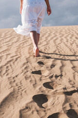 Person walking through the dunes leaving their footprints in the sand. Not recognizable: beach