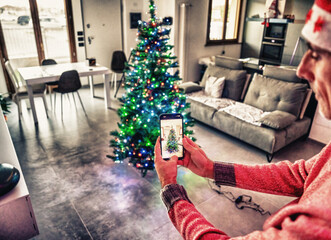 Man using smart home app to decorate and lighting Christmas Tree. Back view