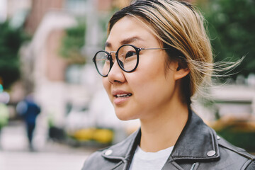 Side view of asian female traveler in eyeglasses standing on street searching way for location...