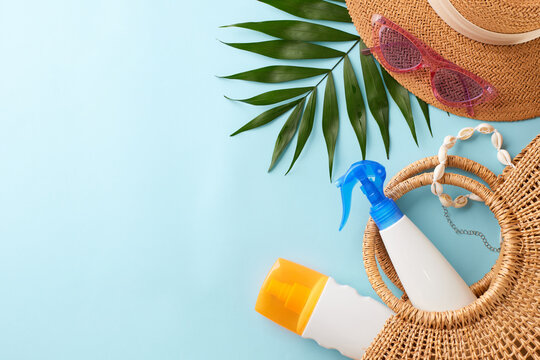 Summer beach essentials including sunscreen and a palm leaf in a wicker bag on a blue background, ideal for vacation themes. Perfect for travel guides, summer product promotions