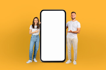 A man and woman are standing beside a blank phone screen, posing for a photo. They both appear to...