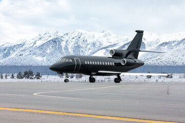 Black luxury business jet on airport apron in winter on the background of high picturesque snow...