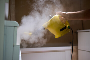 hand in gloves. Using a steam cleaner to clean a washing machine