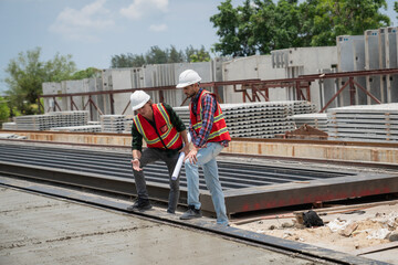 Fototapeta premium Engineer or architect with a hardhat examines the schedule on a set of plans. Two businessmen, both engineers, at the construction site.