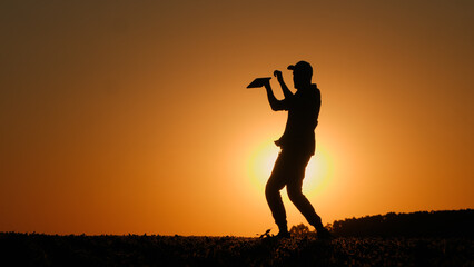 Fototapeta premium A man with a tablet in his hand dances a cheerful dance in a field at sunset