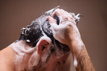 Man washing hair with shampoo in shower, creating foamy lather - personal hygiene care.