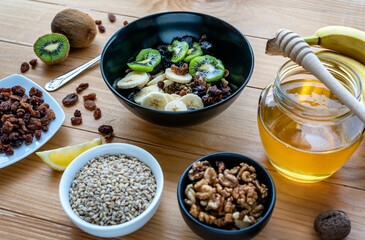 Healthy breakfast. Soaked organic raw barley, walnuts, kiwi, banana, raisins, prunes and honey on the table, wooden background
