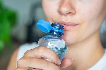 Young woman drinking from a bottle with stationary plastic cap. The new design means the cap remains attached to the bottle after opening, making the entire package easier to collect and recycle