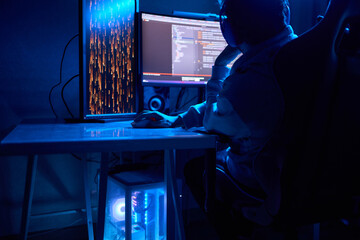 A coder is working late at night on a computer screen, coding and using a smartphone app