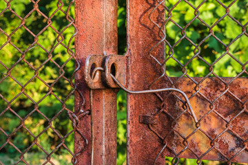 An old rusty iron Wicket gate is closed with wire. Rural iron gate close up