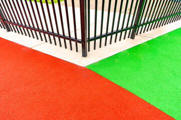 Close-up photo of an ornamental black metal fence surrounding a multi color playground surface.	