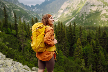A smiling female traveler with a yellow hiking backpack enjoys the beautiful scenery of the...