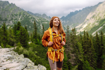 A smiling female traveler with a yellow hiking backpack enjoys the beautiful scenery of the...