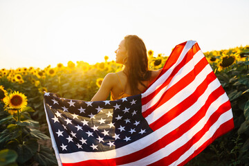Beautiful woman with the American flag in a sunflower field. Freedom day. Independence Day. 4th of...