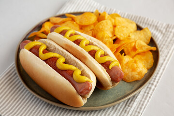 Homemade Hot Dog with Mustard and Potato Chips on a Plate, side view.