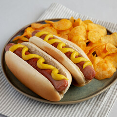 Homemade Hot Dog with Mustard and Potato Chips on a Plate, side view.