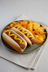 Homemade Hot Dog with Mustard and Potato Chips on a Plate, side view.