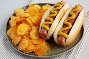 Homemade Hot Dog with Mustard and Potato Chips on a Plate, side view.