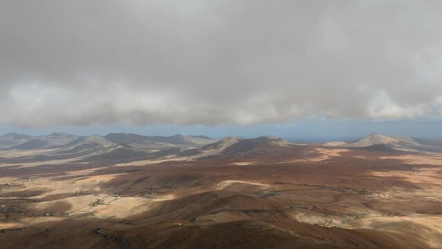 Gray clouds moving cast shadows over the mountains of the windy island of Fuerteventura in the Canary Islands in a far view from above