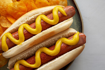 Homemade Hot Dog with Mustard and Potato Chips on a Plate, top view. Close-up.