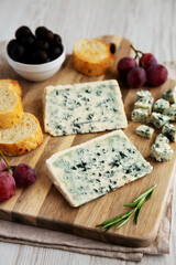 Organic Blue Cheese with Grapes and Olives on a Wooden Board, side view.