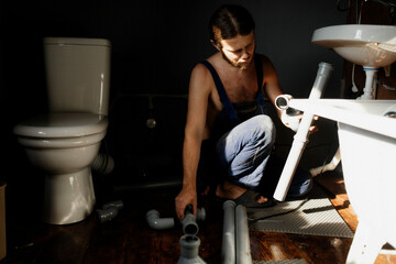 young man plumber is fixing a sewer in the bathroom. A man works at home.