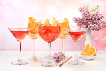 Festive alcoholic cocktail Aperol spritz and red martini in glasses on a bright background with a bouquet of lilacs, summer bar concept, alcoholic drinks at a party, restaurant and cafe advertising,