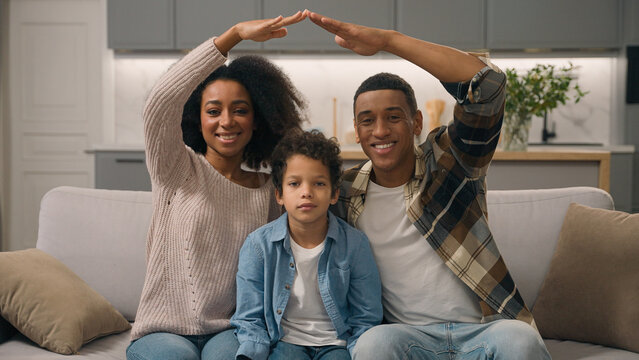 Smiling joyful African American ethnic family young happy homeowners mother father hands showing roof gesture little son boy child kid posing looking camera inside new home. Housing buying real estate