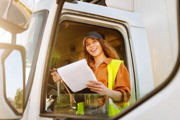 Portrait of beautiful young woman professional truck driver sitting in a big truck. People and...