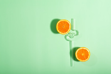 There are two slices of orange and a glass straw set on a green background