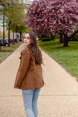 A beautiful young woman turned to look, with a cherry blossom tree behind her 