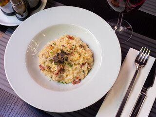 Authentic Italian style mushroom risotto with ham slices served on white plate with fresh greens