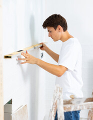 Man measuring flatness of wall with spirit level tool in new apartment during renovation